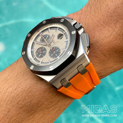 Angled wrist view of an AP Royal Oak Offshore 26400 fitted with an orange replacement rubber strap beside a swimming pool.